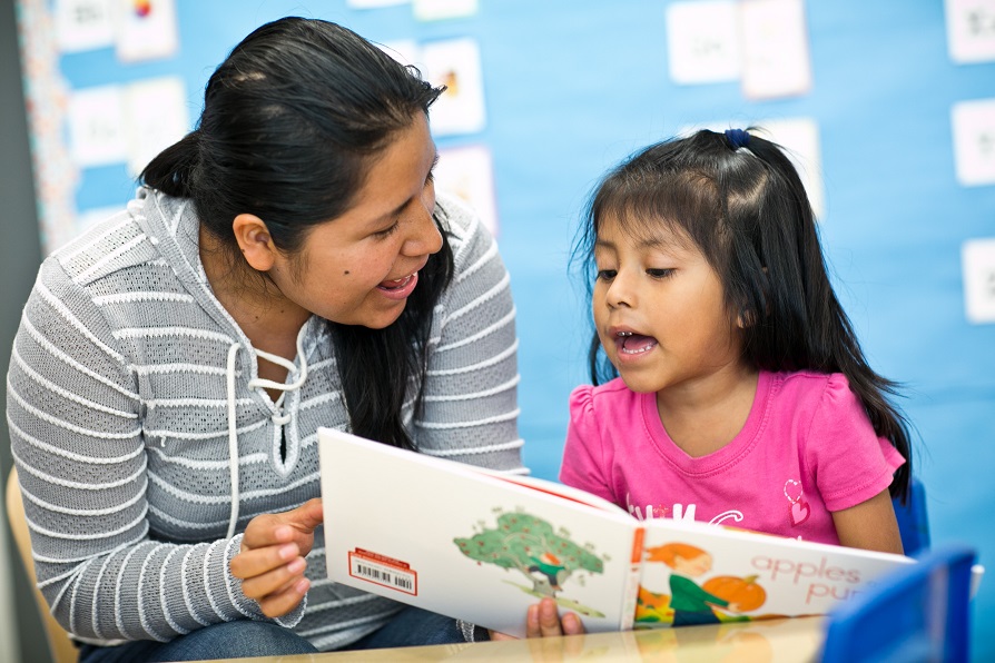 Mother and daughter smile as they read a book together.