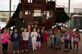 Trent Sneed, Wells Fargo Museum Curator, joins Hope Street children in front of an original Wells Fargo stagecoach.