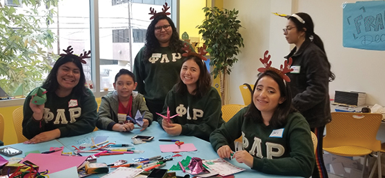 Five ladies from Phi Lambda UCLA make holiday cards with a young Hope Street boy