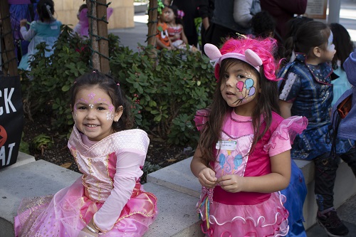 Two little girls dressed in pink Halloween costumes smile for the camera.